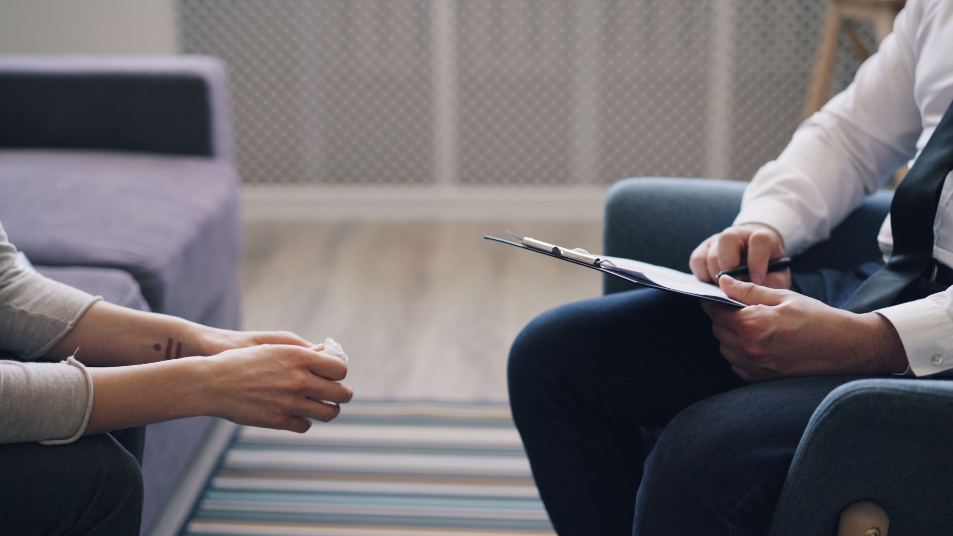 A counselor with a clipboard sits facing a client during a one-on-one session in a calm office