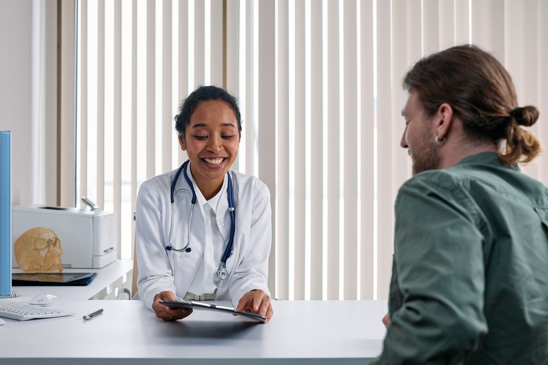 A smiling doctor at her desk shows a tablet to a young man sitting across from her