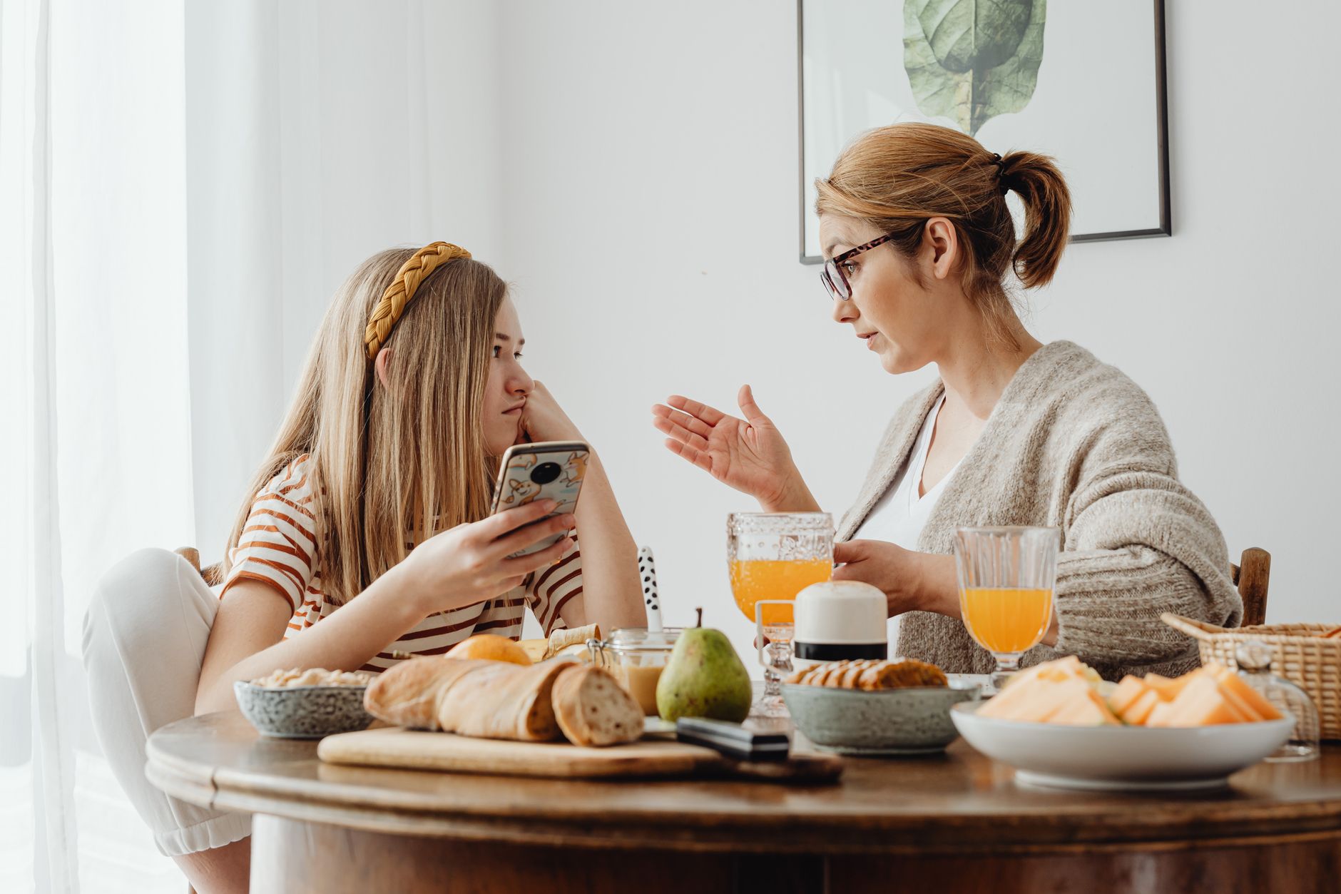 A mother talks with her teenage daughter across a breakfast table at home
